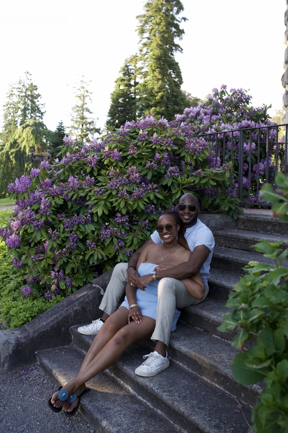 Sally and Adetunji sitting together on the garden steps beside a rhododendron in bloom
