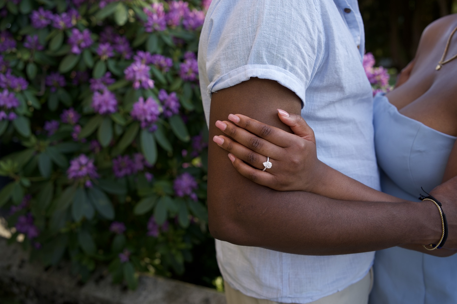 Sally's ringed hand resting on Adetunji's arm among the purple blossoms
