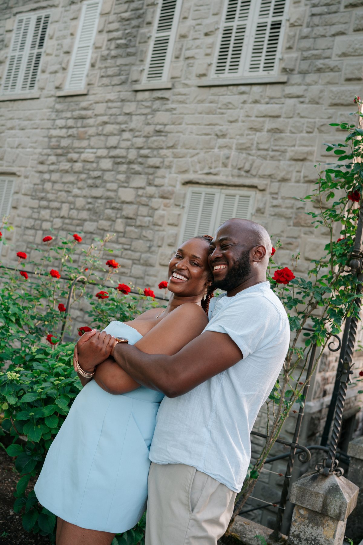 Adetunji and Sally by a wall of red roses at golden hour